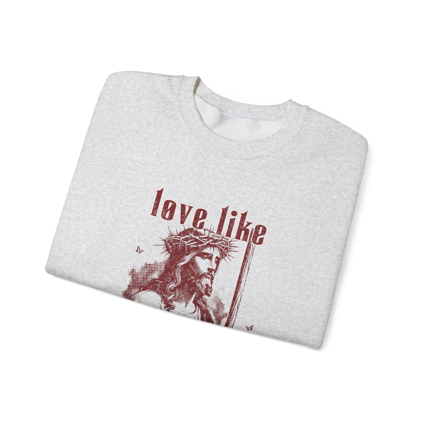 Folded gray t-shirt with a graphic of a person wearing a crown of thorns and text 'love like' on a white background
